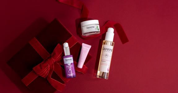 Produkty pielęgnacyjne lavera z czerwonym pudełkiem prezentowym na ciemnoczerwonym tle