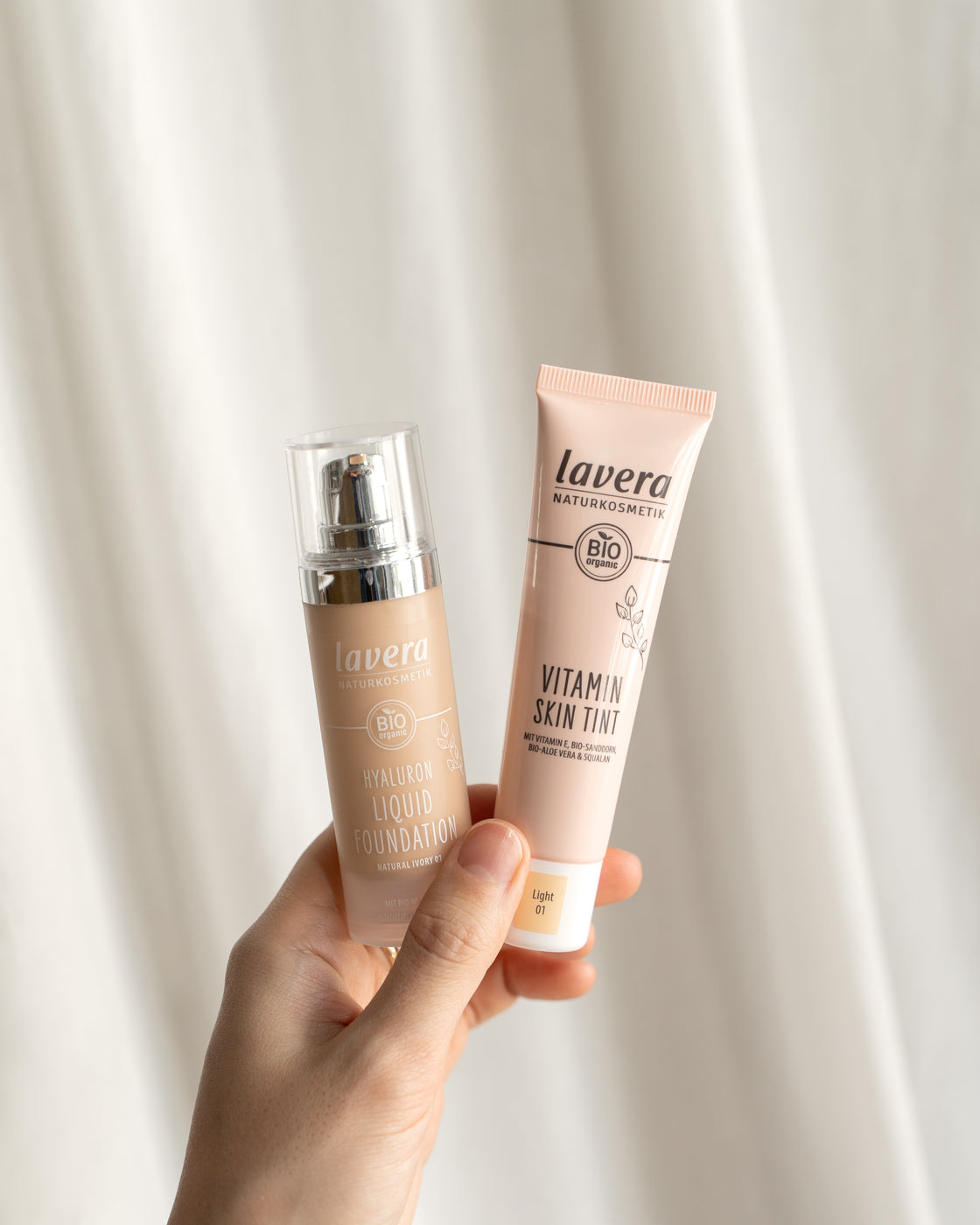 Hand hält Hyaluron Liquid Foundation und Vitamin Skin Tint