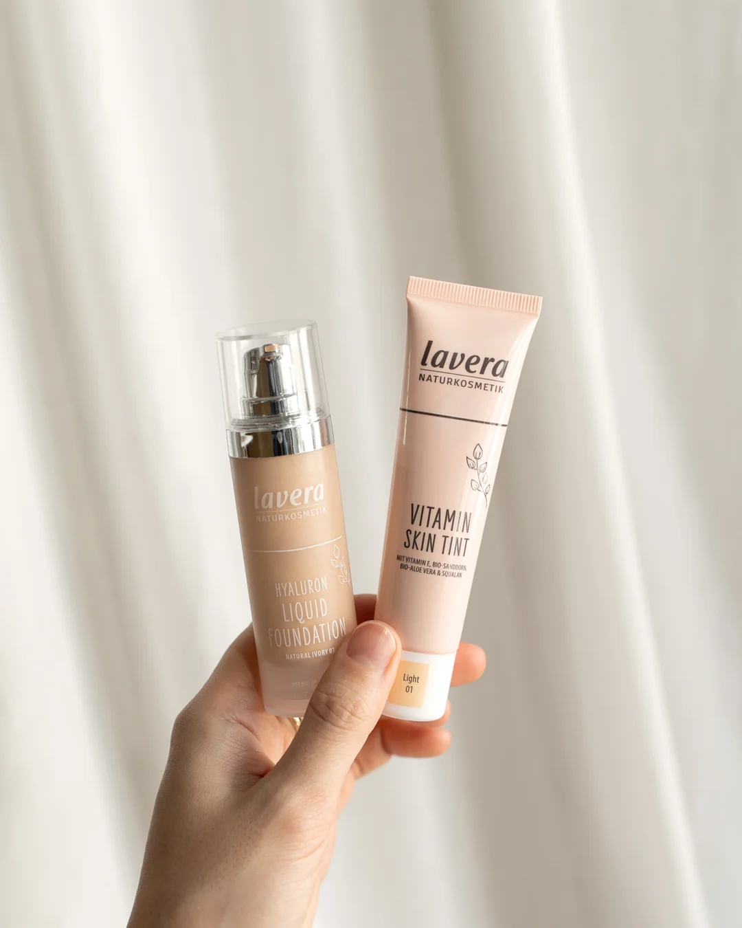 Hyaluron Liquid Foundation und Vitamin Skin Tint in der Hand gehalten