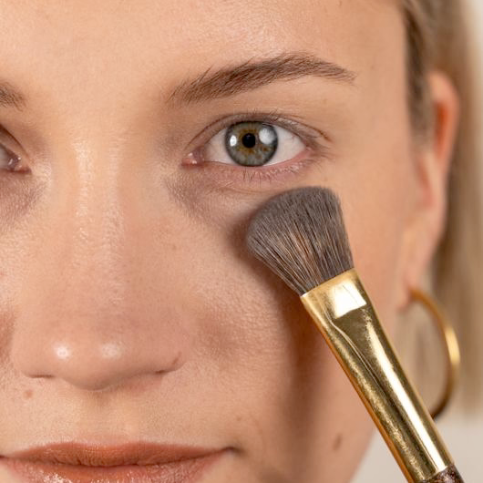 Make-up-Pinsel trägt Puder unter dem Auge auf, Nahaufnahme Gesicht