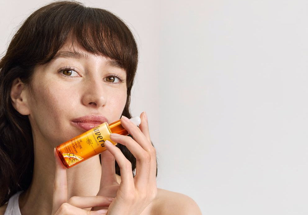 Frau hält lavera Serum an die Wange im Studio