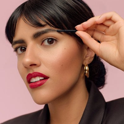 Kobieta szczotkuje swoją brew szczoteczką na różowym tle