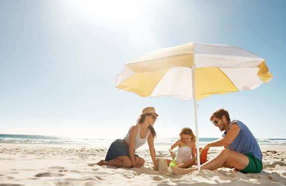Rodzina z dzieckiem pod parasolem na plaży podczas zabawy w piasku