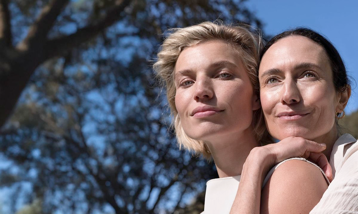 Dwie kobiety w słońcu, jedna obejmuje drugą, naturalny wygląd na zewnątrz