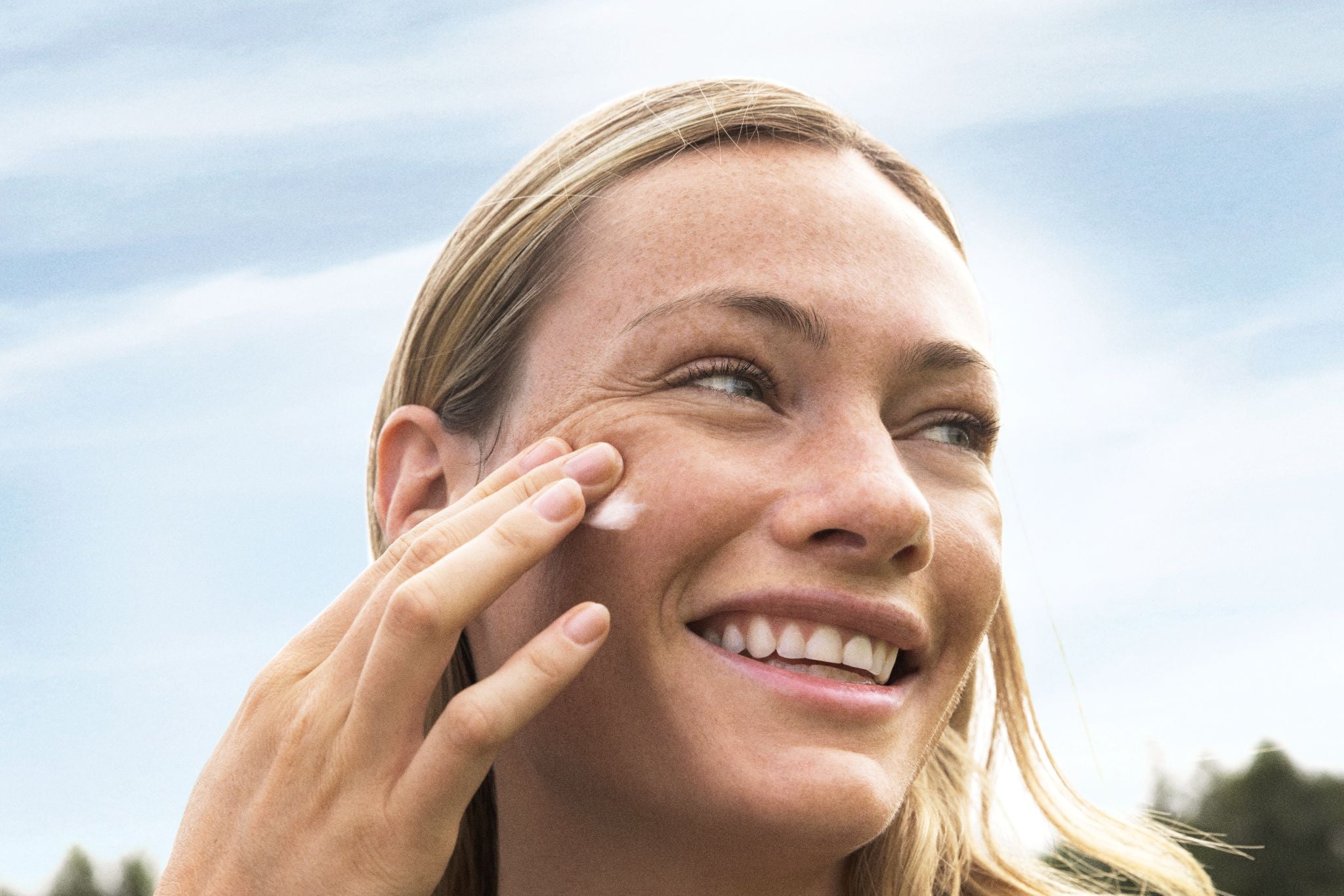Frau in der Natur trägt die Creme auf das Gesicht auf