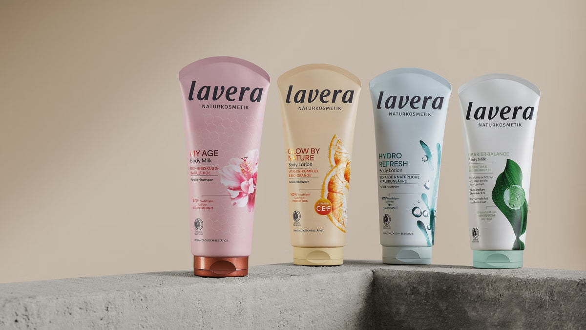 Cztery balsamy do ciała lavera z linii My Age, Glow by Nature, Hydro Refresh i Barrier Balance stoją na szarych betonowych cokołach na neutralnym tle.