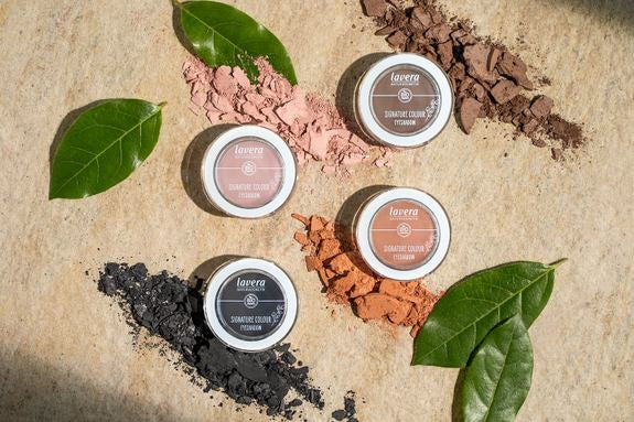 Vier lavera Lidschatten mit Farbpigmenten und grünen Blättern dekoriert