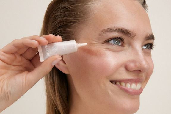 Lächelnde Frau trägt ein Hydrating Fluid auf ihre Wange auf