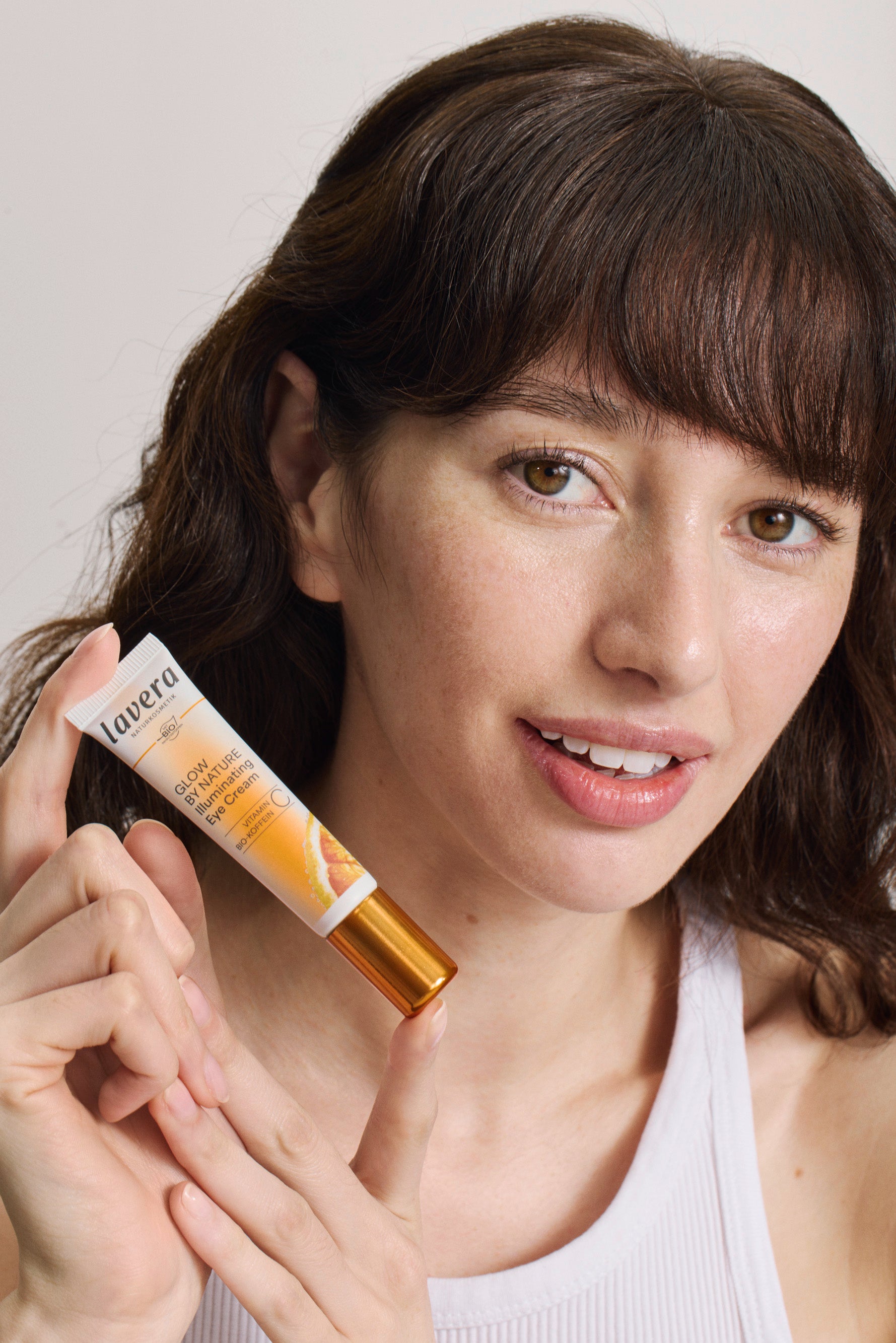Eine Frau hält die lavera Glow by Nature Illuminating Eye Cream in der Hand
