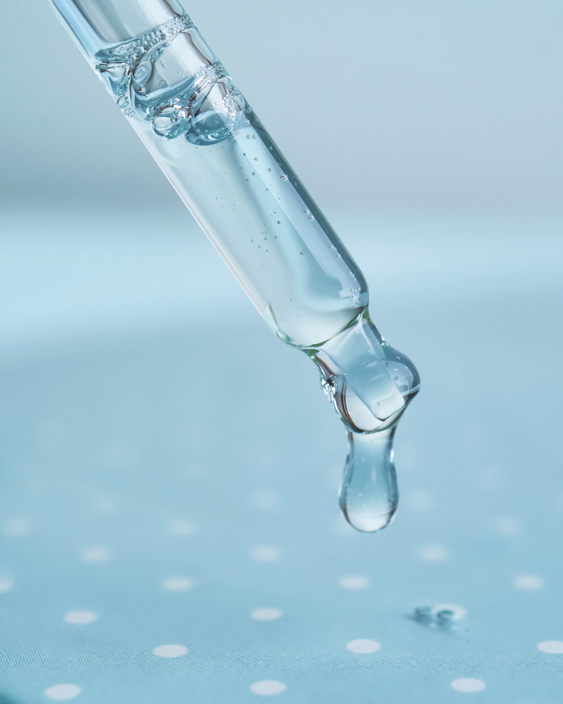 Pipeta upuszczająca przezroczystą kroplę serum, makro na niebieskim tle