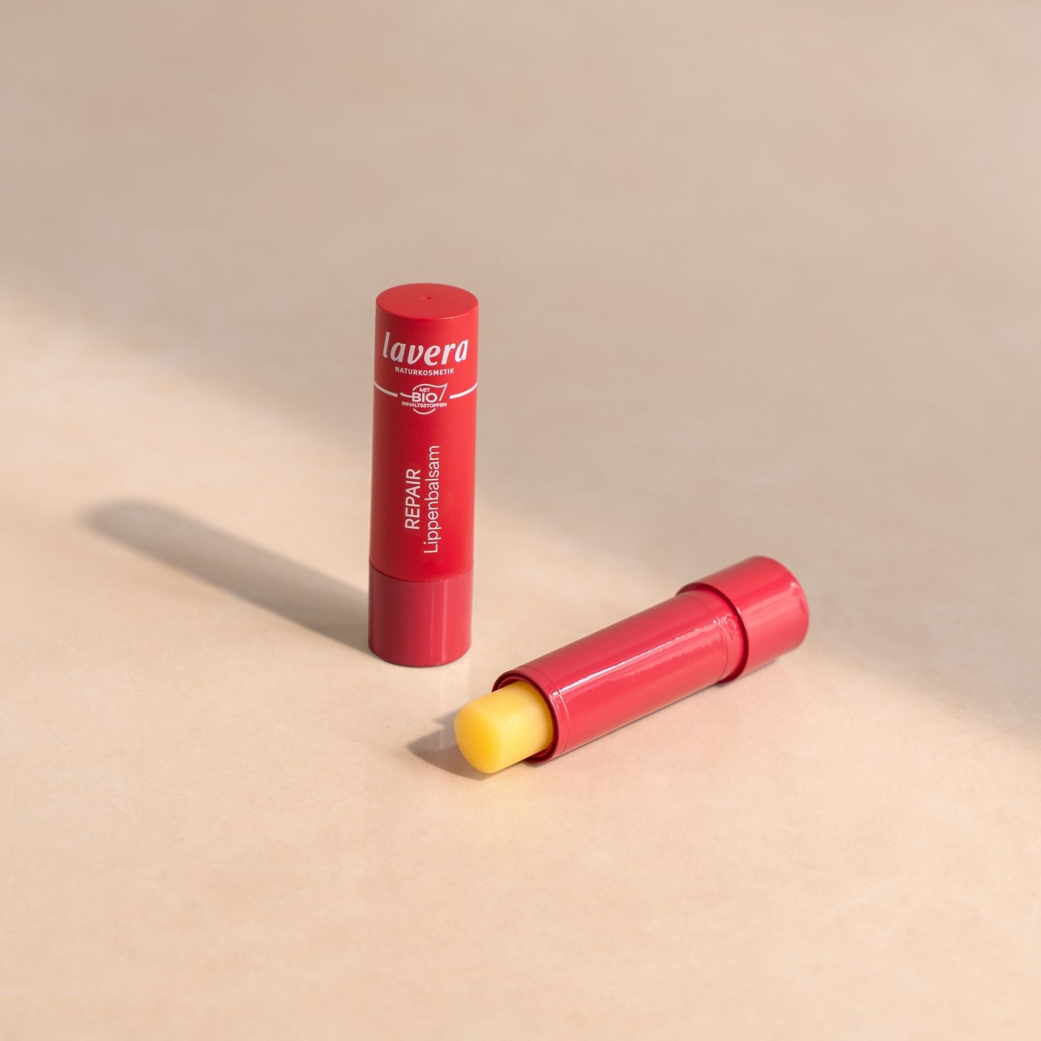 zwei Lavera Repair Lippenbalsame in roter Verpackung, geöffnet und geschlossen auf hellem Untergrund.