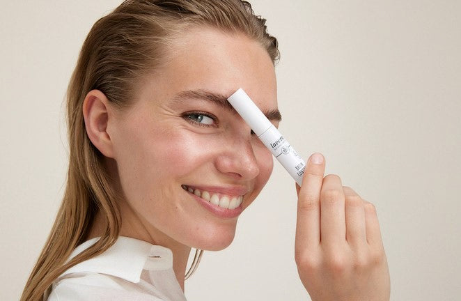 Lächelnde Frau hält lavera Augenbrauenstift an die Braue, Nahaufnahme