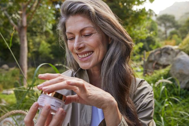 Reife Frau öffnet My Age Creme-Tiegel im Grünen