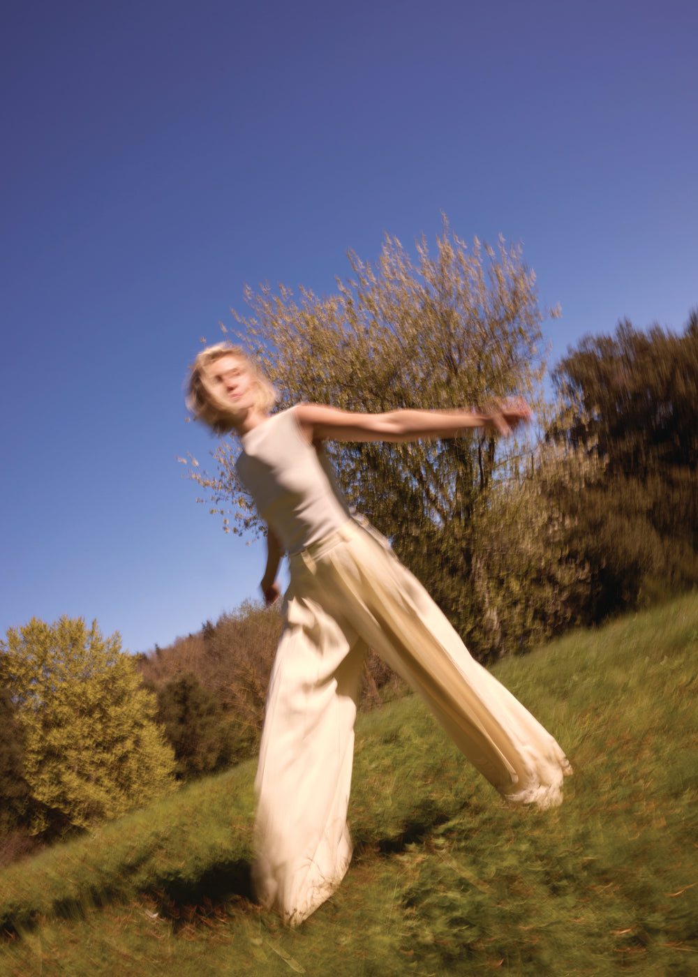 Frau in beigefarbenem Kleid dreht sich mit ausgebreiteten Armen in der Natur – Ausdruck von Lebensfreude und innerer Balance