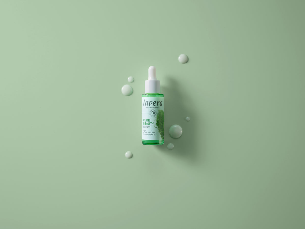 Das lavera Pure Beauty Serum mit Tropfen des Serums auf grünem Hintergrund.