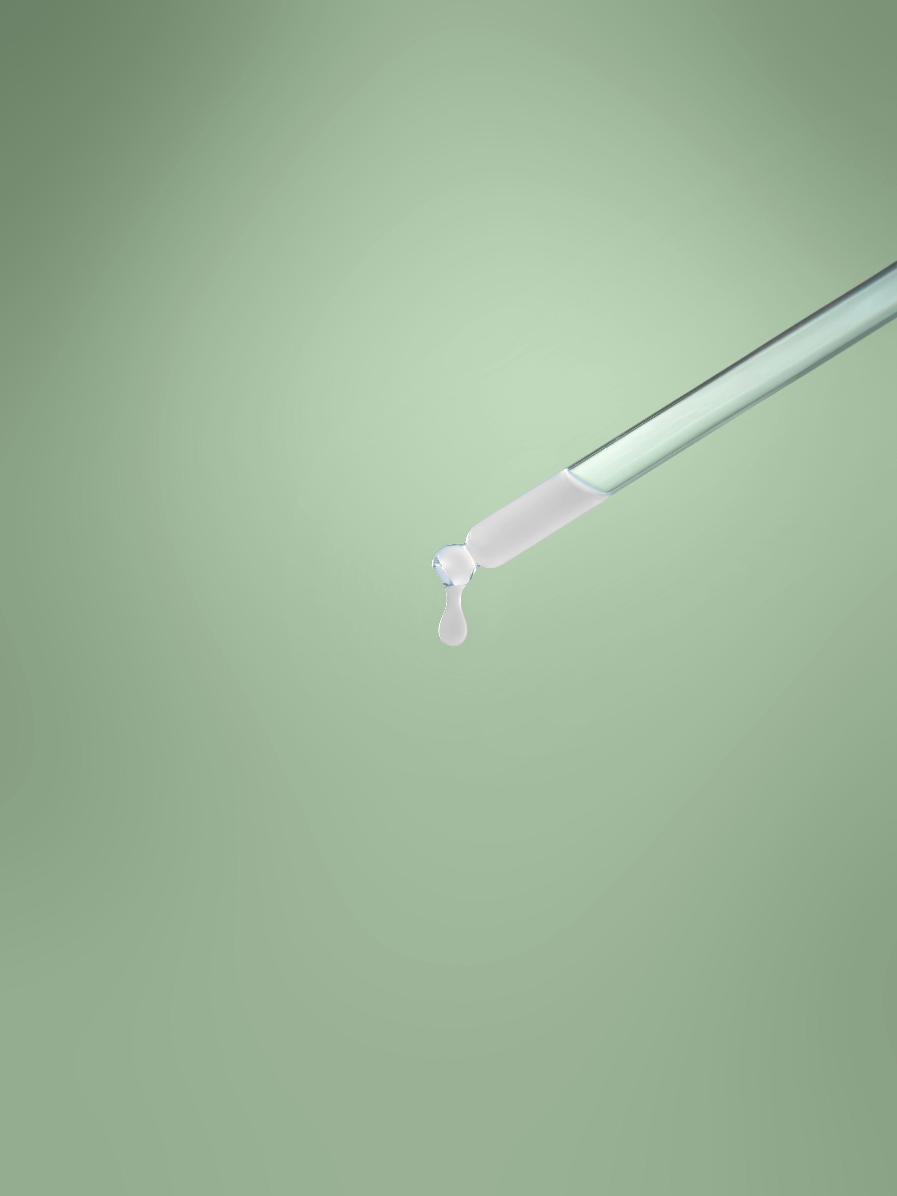 Eine Pipette mit Gesichtsserum gefüllt vor grünem Hintergrund