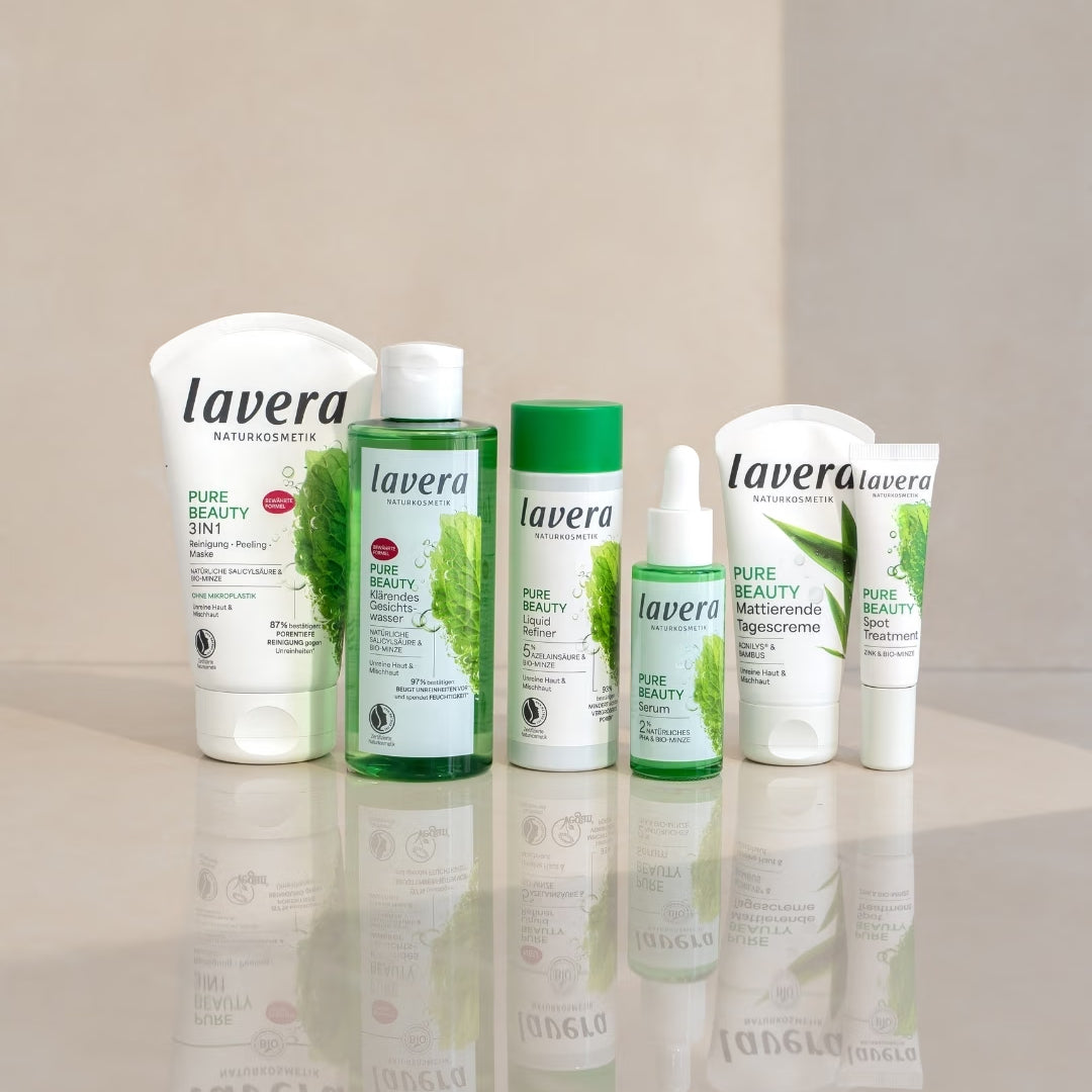 Produkty do pielęgnacji twarzy lavera Pure Beauty stoją na lustrzanej powierzchni przed jasnym, podzielonym na dwie części tłem.