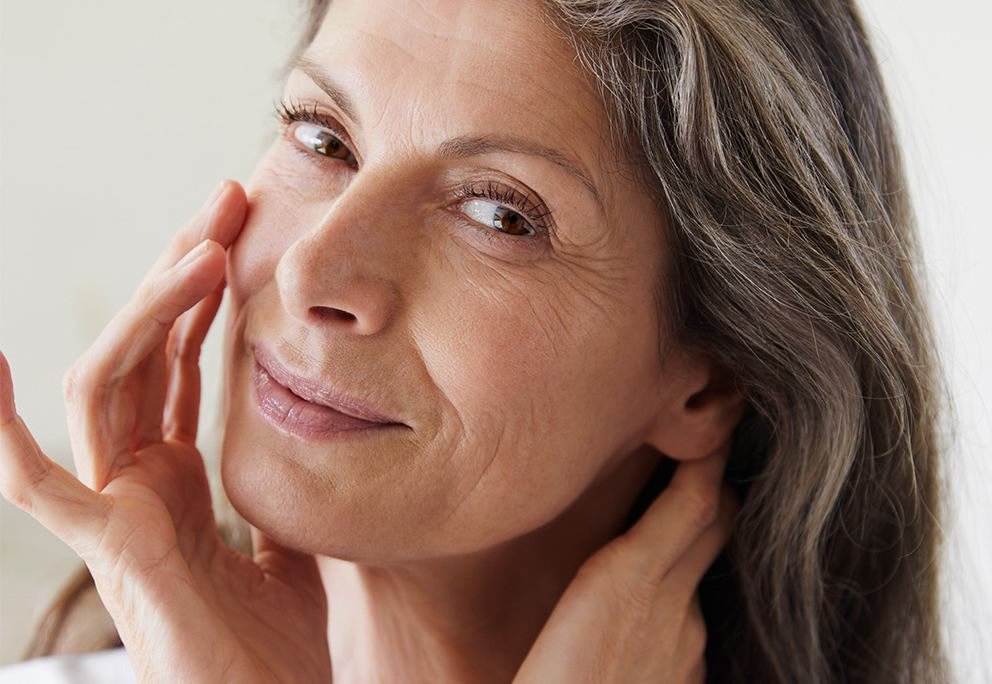 Portret: Kobieta z siwymi włosami dotyka policzka i szyi, uśmiecha się