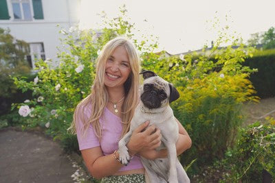 Blond kobieta uśmiecha się i trzyma mopsa w ramionach