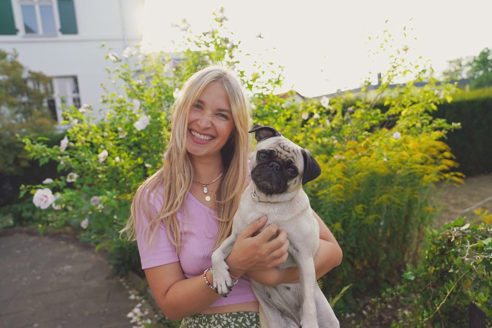 Blond kobieta uśmiecha się i trzyma mopsa w ramionach
