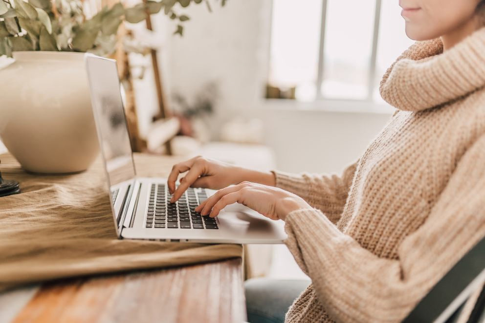 Frau im Strickpullover tippt am Laptop am Holztisch, gemütliches Zuhause