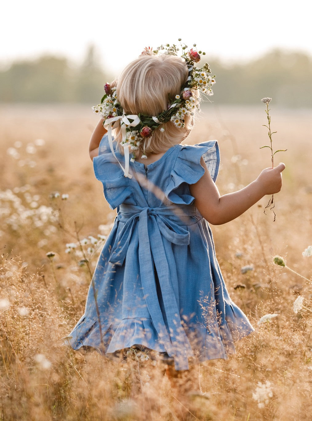 Ein Mädchen trägt einen Gänseblümchenkranz auf dem Kopf und geht den Field entlang