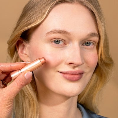 Młoda kobieta o blond włosach uśmiecha się do kamery i nakłada kolor na policzek