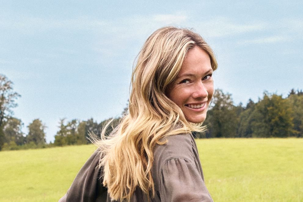 Blond kobieta uśmiecha się przez ramię na zielonej łące, portret plenerowy